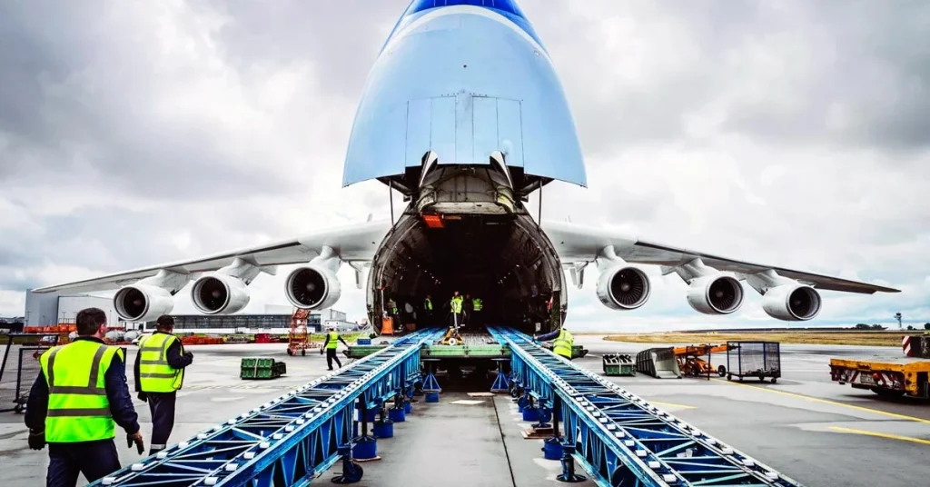 Ground crew loading cargo into the open nose of a large white airplane via a blue conveyor belt, representing the process of getting an air freight quote.