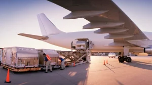 Du personnel au sol chargeant des conteneurs de fret à bord d’un grand avion blanc dans un aéroport, illustrant le choix entre le fret aérien express en provenance de Chine et le fret aérien général.